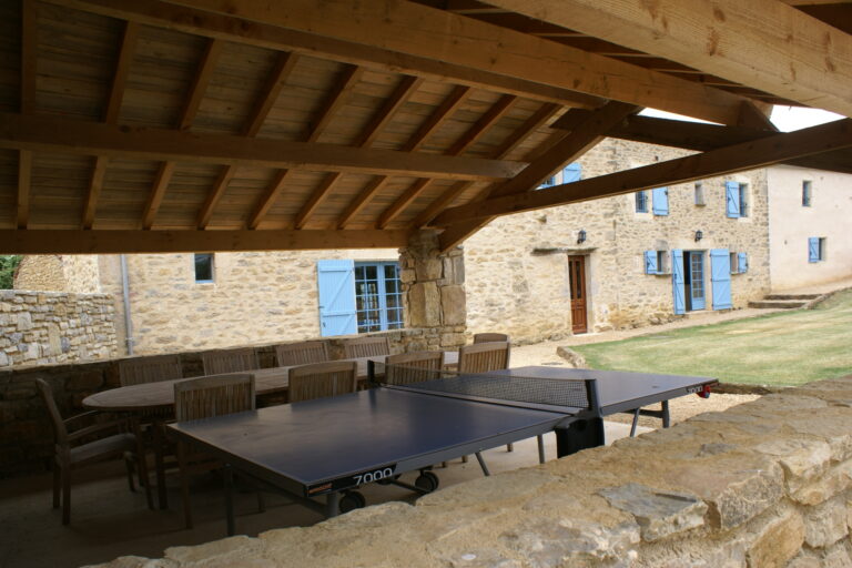The full-size table tennis table under the open barn, with the farmhouse beyond