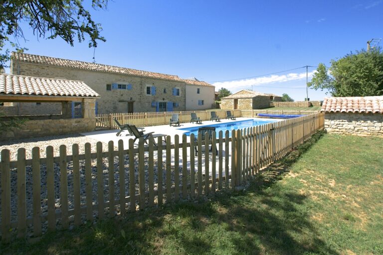 La Vieille Ferme and its covered barn seen from the garden, with the fenced swimming pool between them