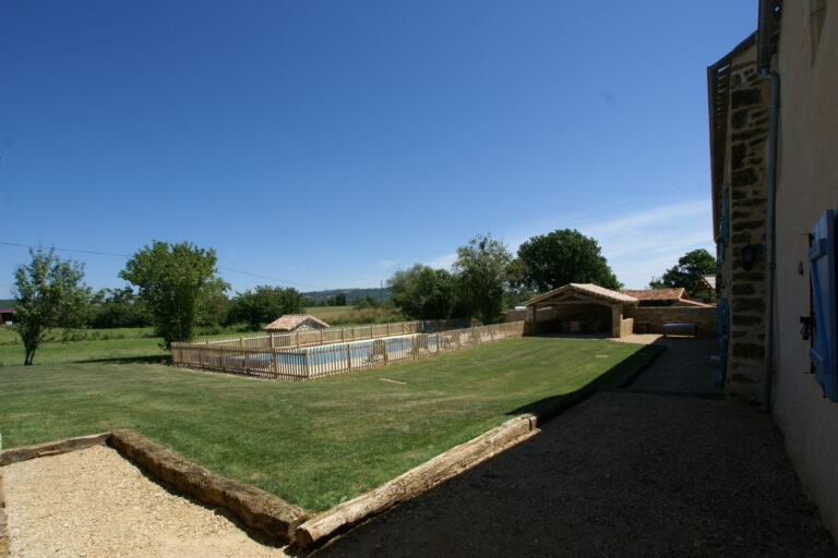 The lawn sloping down to the fenced swimming pool and open barn, with open countryside beyond