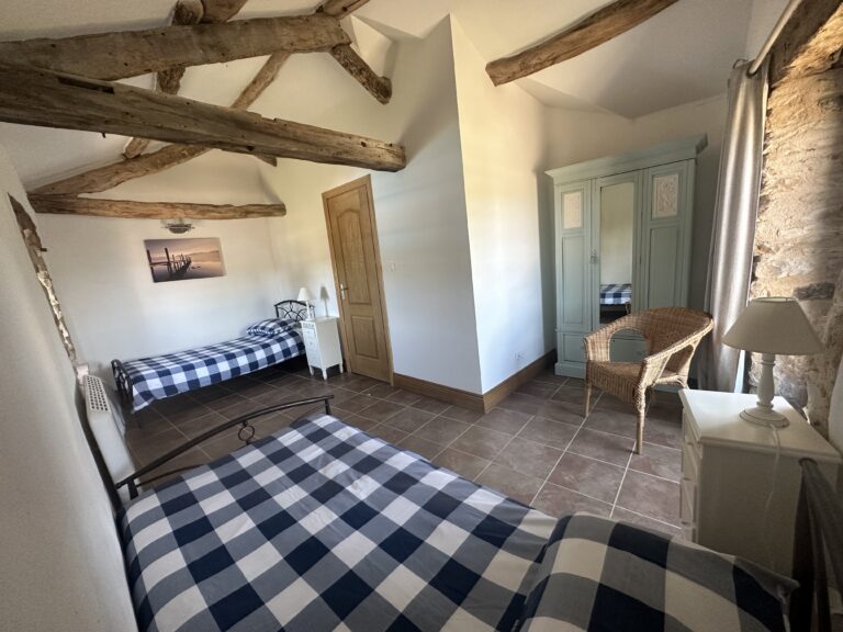 Bedroom 4, a twin room under exposed A-frame roof timbers, with a painted wardrobe, wicker chair and exposed stone wall