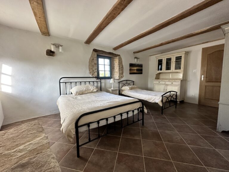 Bedroom 6 on the ground floor, with a double bed and a single bed under beamed ceilings, a deep stone window and a painted dresser